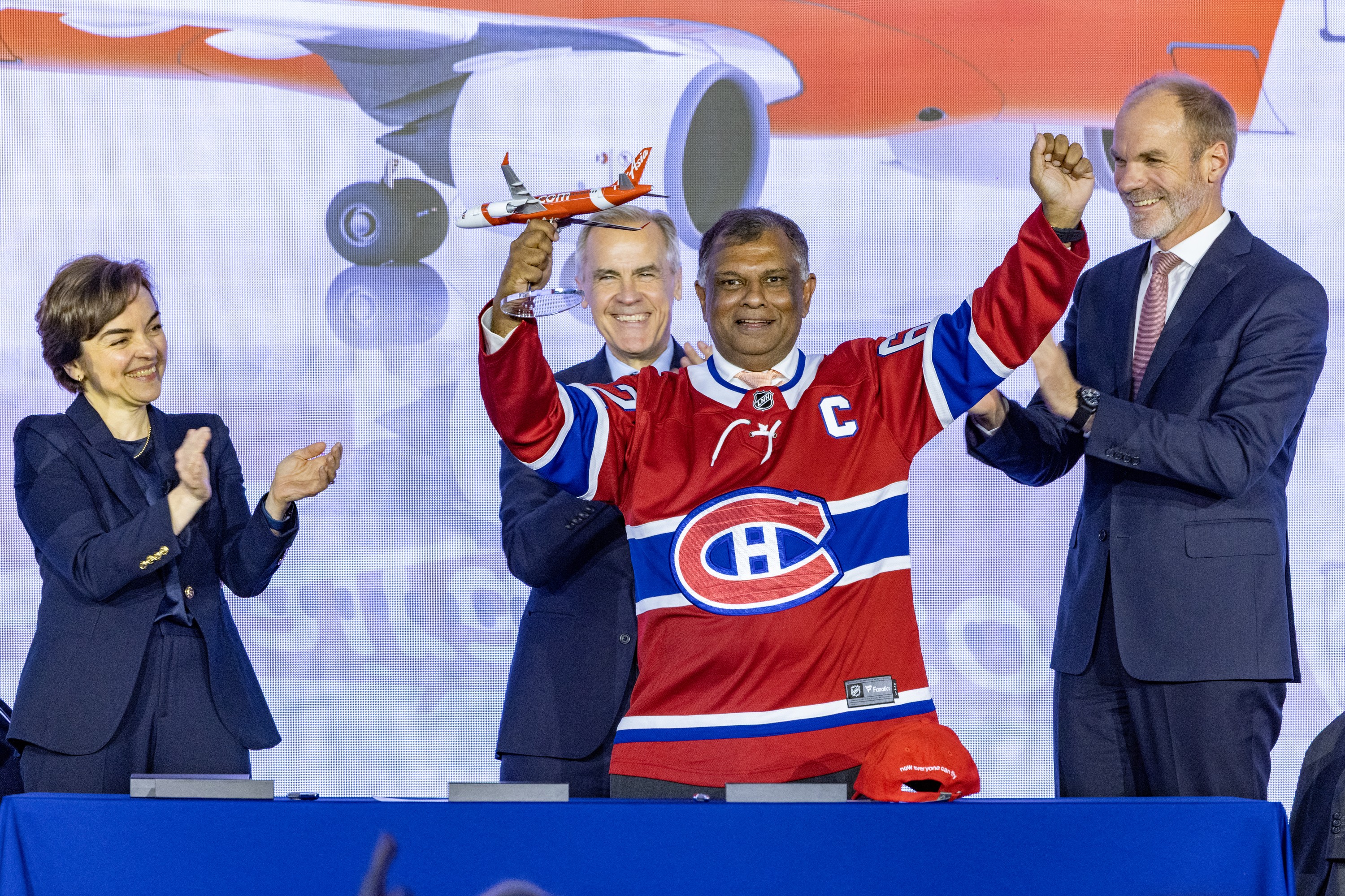 Lars Wagner, right, Chief Executive Officer of the Commercial Aircraft Business, Prime Minister Mark Carney and Quebec Premier Christine Fréchette applaud as Air Asia CEO Tony Fernandes wears a Montreal Canadiens jersey 