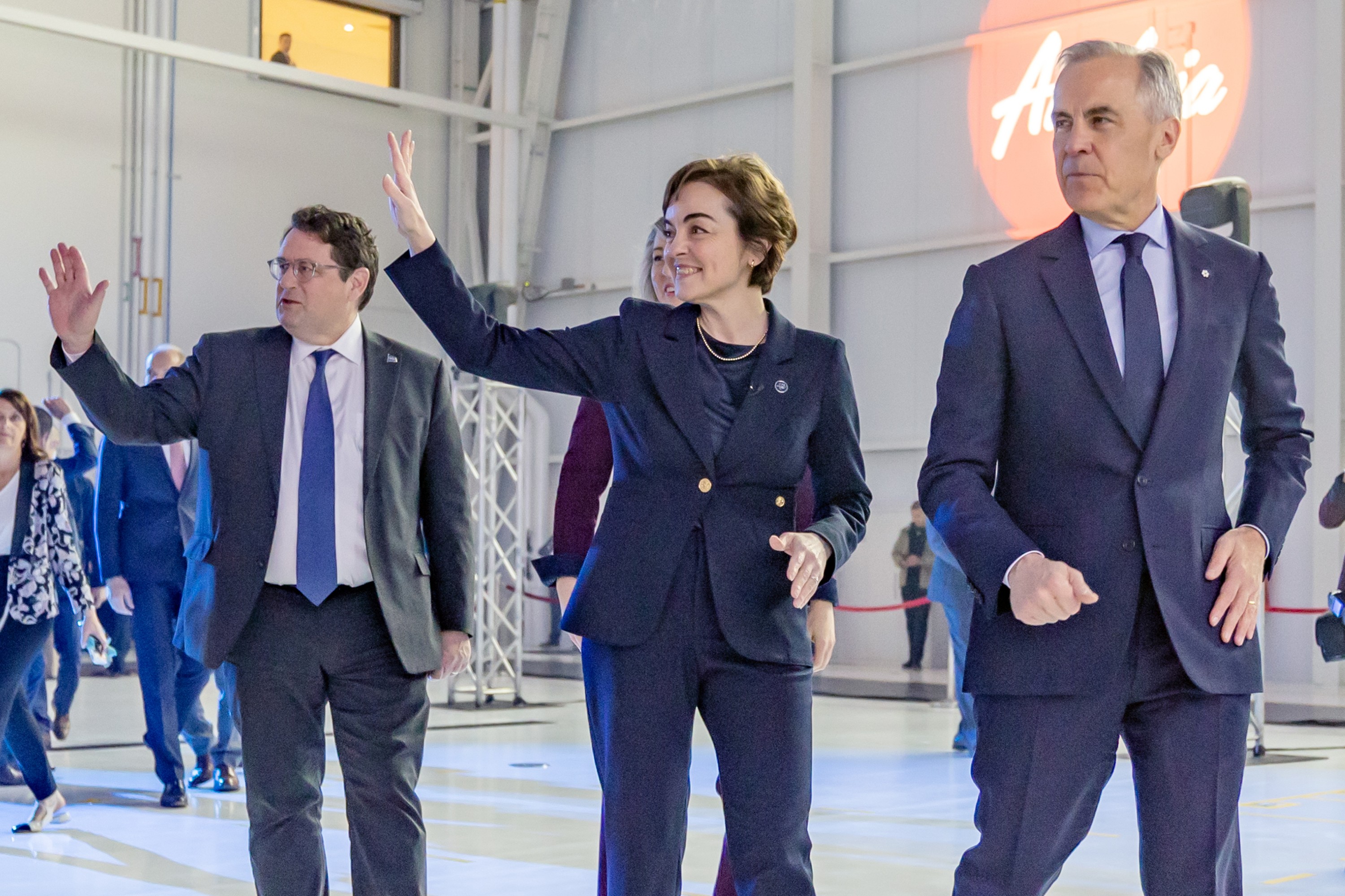 Four people walk in a large room waving to people