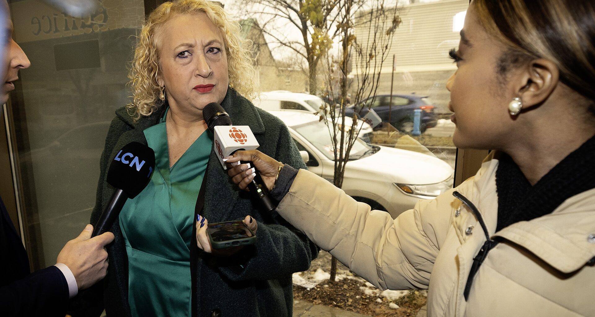 A woman is confronted by two journalists holding microphones.