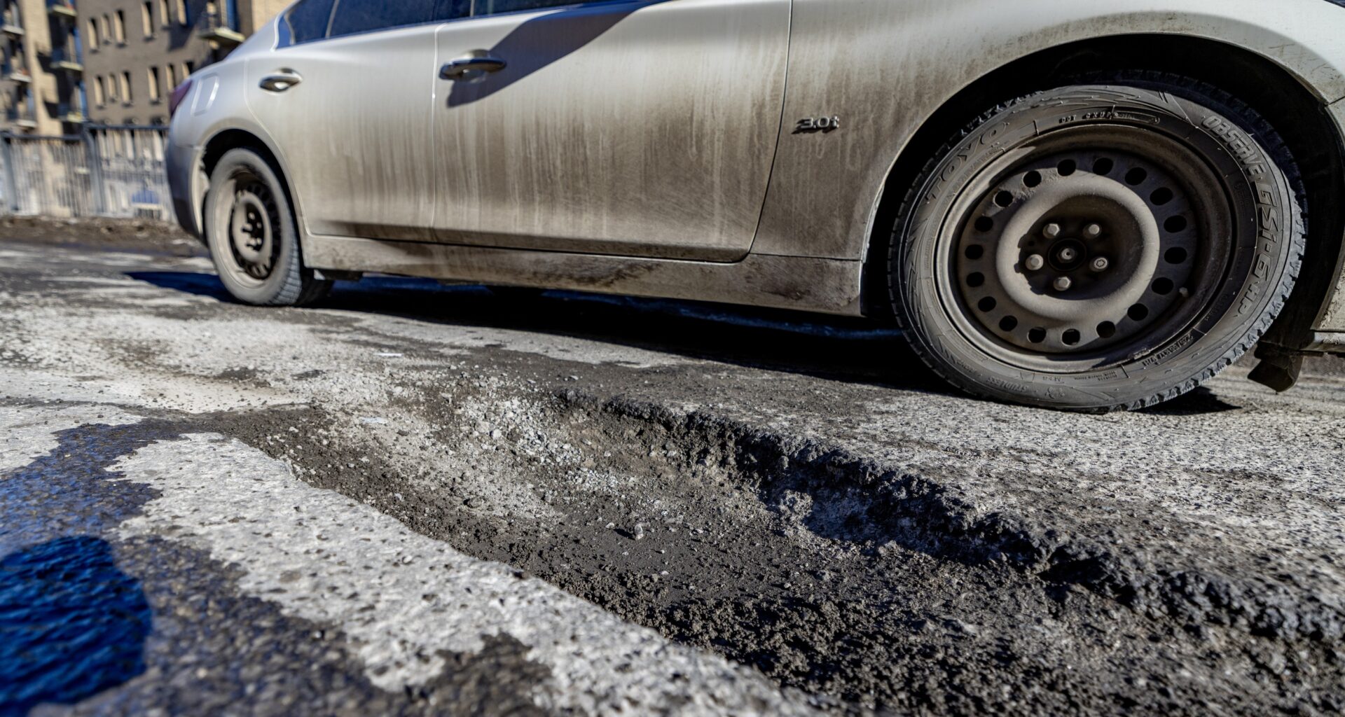 Car drives by big pothole on Montreal road.