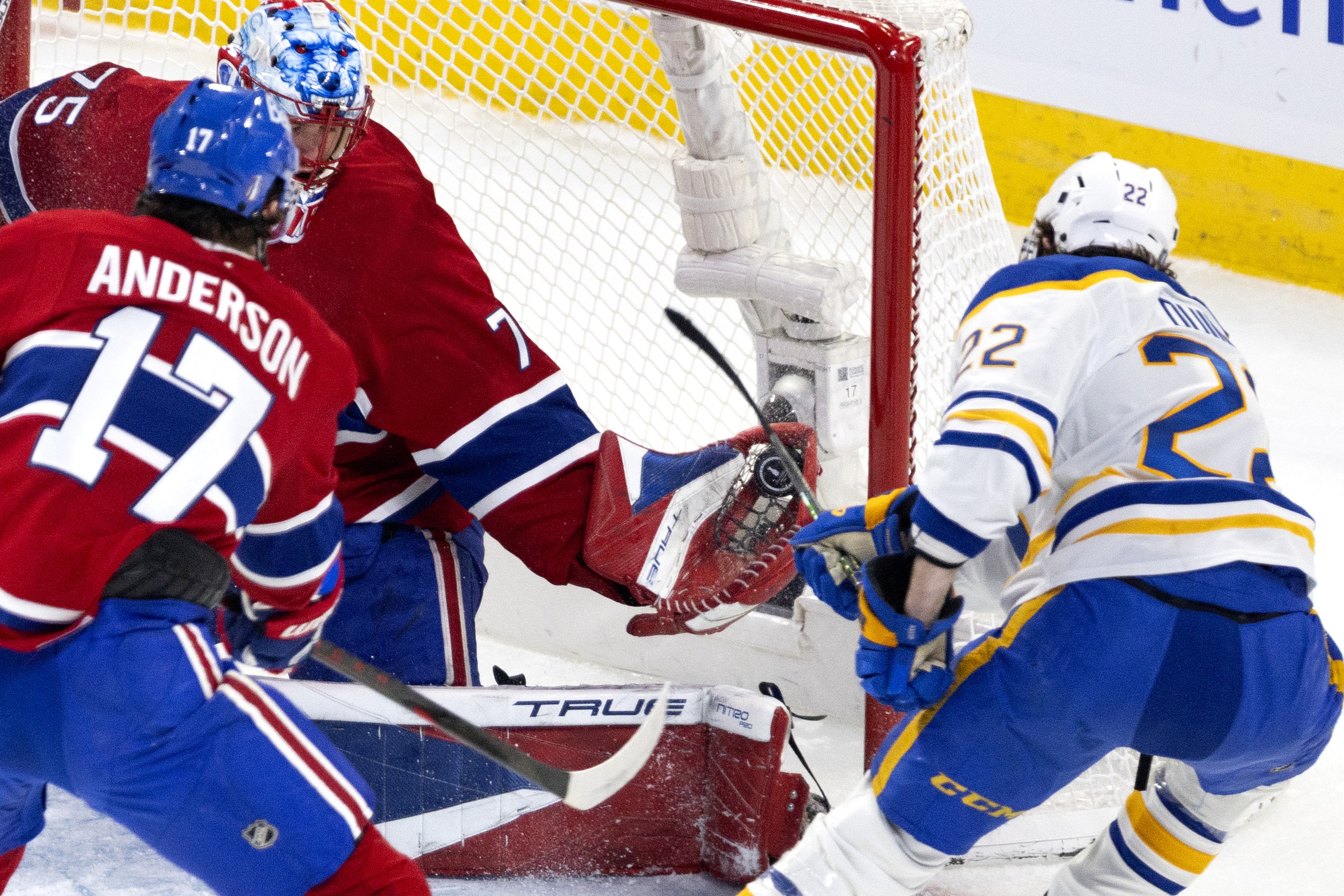 Canadiens Jakub Dobes gloves a puck in the net as a Sabres player follows through on a shot from close range.