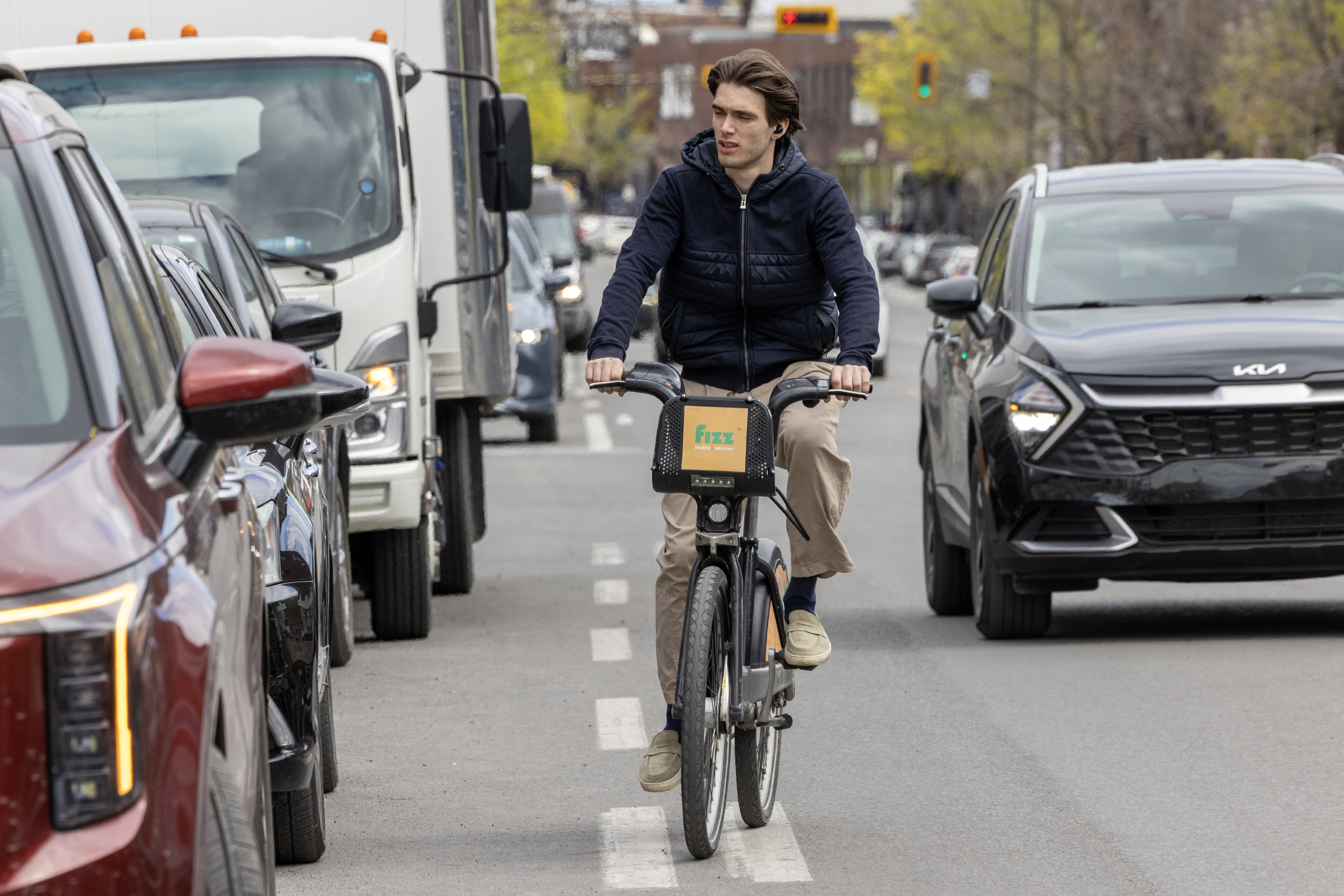 Young man riding a bike on busy thoroughfare.