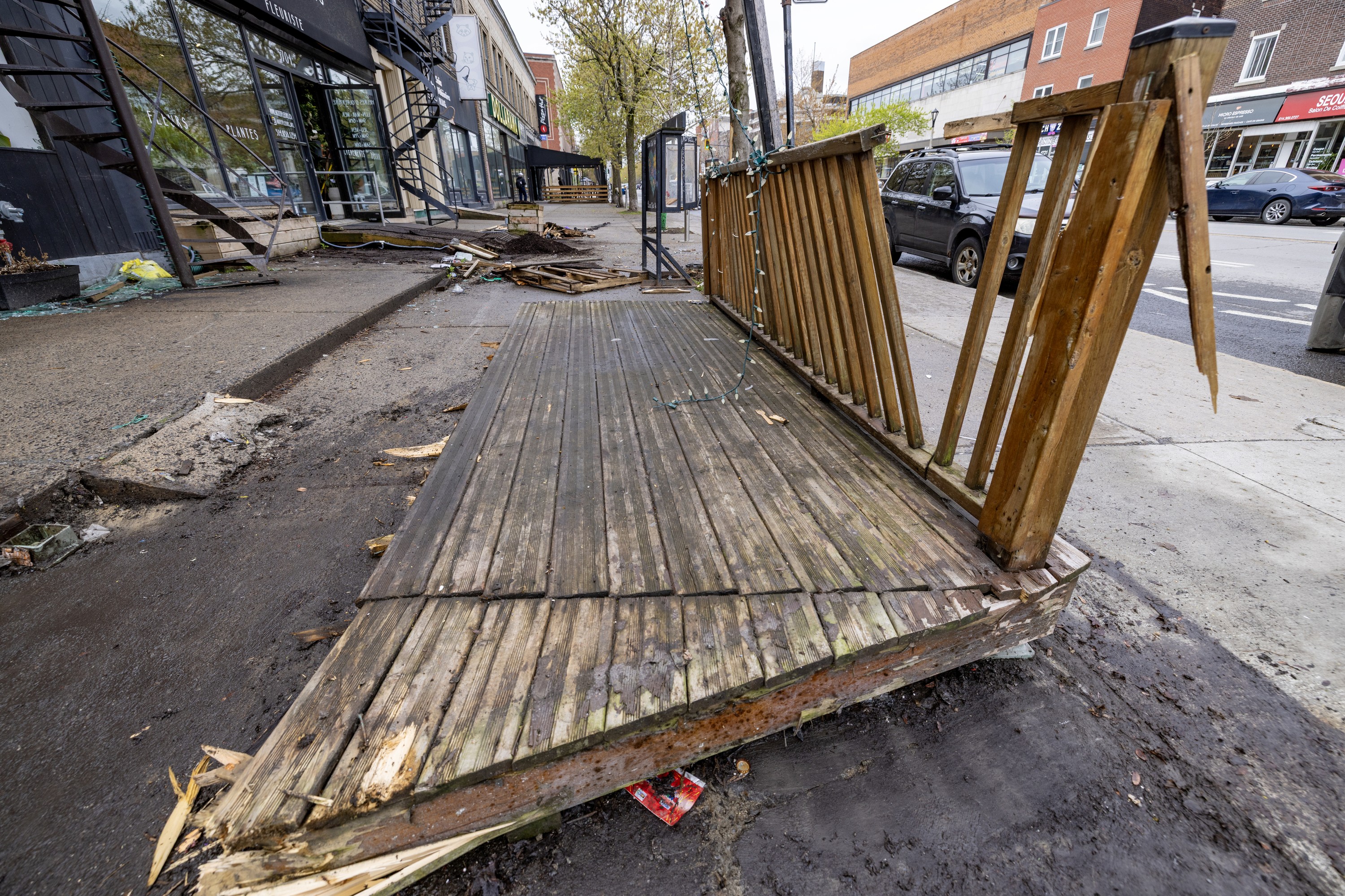 Broken parts of wooden railing and floor near a sidewalk.