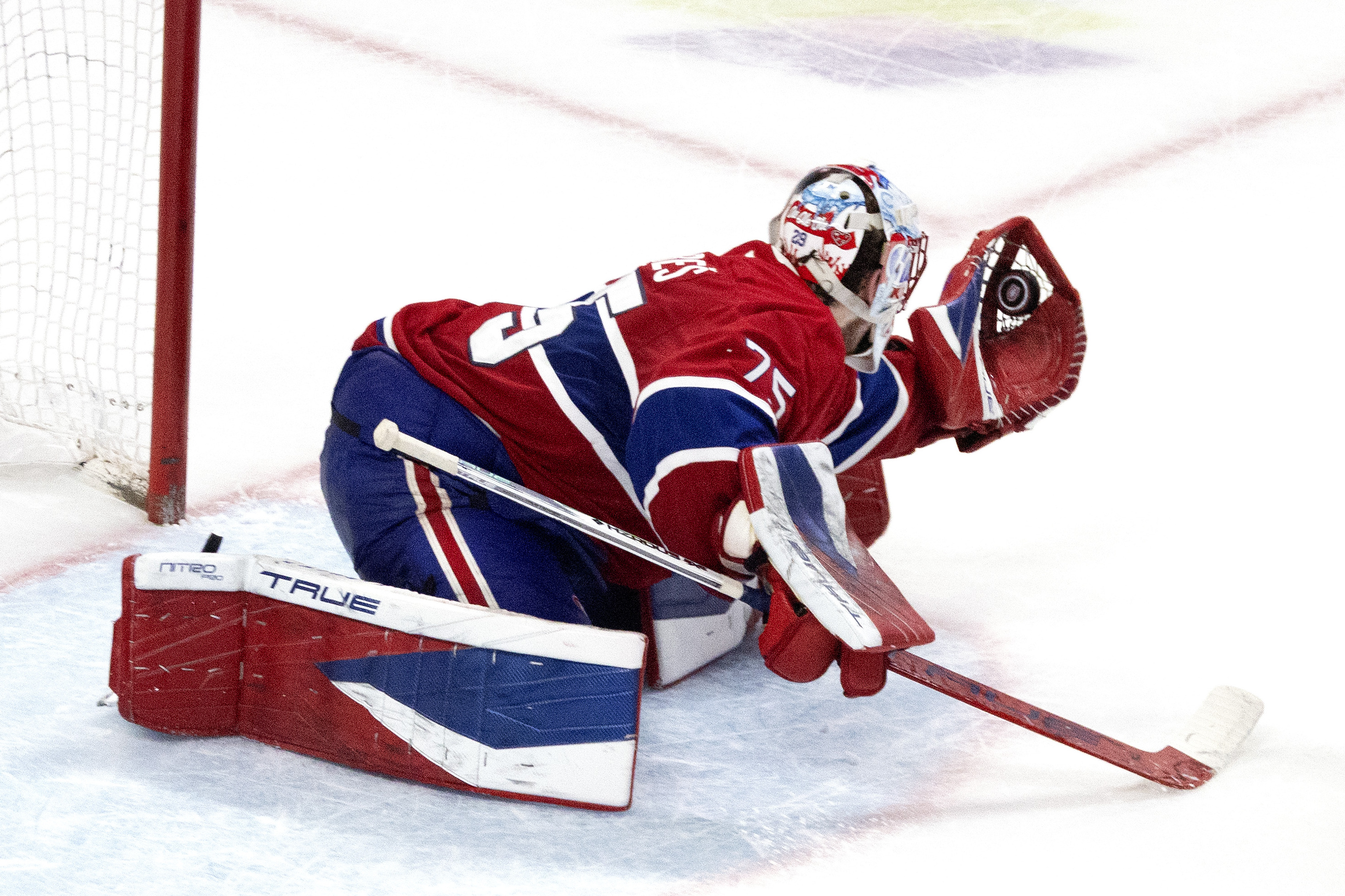 Hockey goaltender makes a save with his glove with his knees on the ice. 