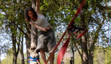 A woman balances on a tightrope held between two trees in a park.