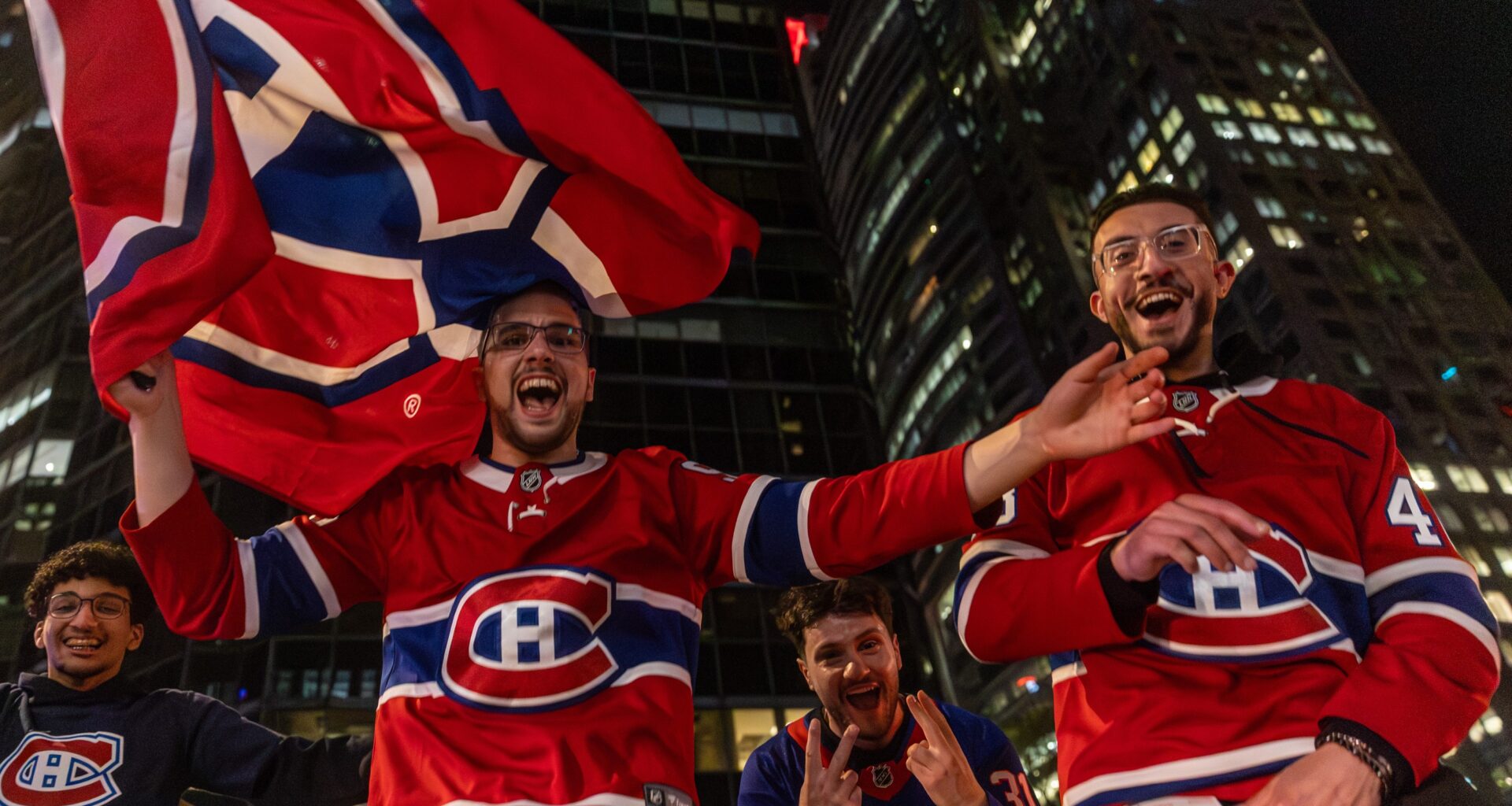 People in Canadiens jerseys and carrying Canadiens flags cheer on a street outside at night.