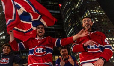 People in Canadiens jerseys and carrying Canadiens flags cheer on a street outside at night.