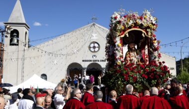 A crowd of people, some in religious garb, surround a statue of Jesus amid flowers that is being held aloft outside a church.