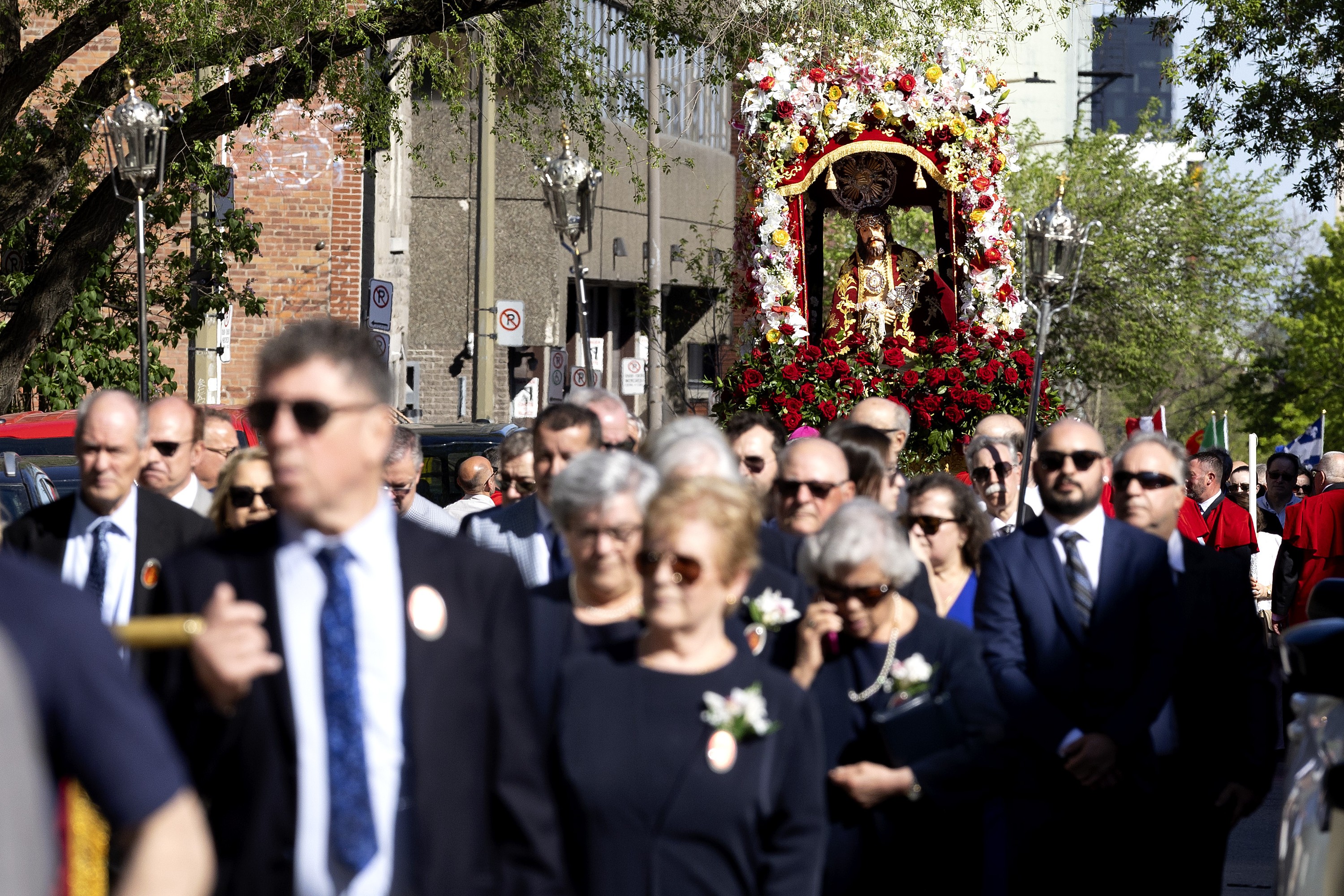 A crowd of people in formal attire lead a raised statue of Jesus through a street.