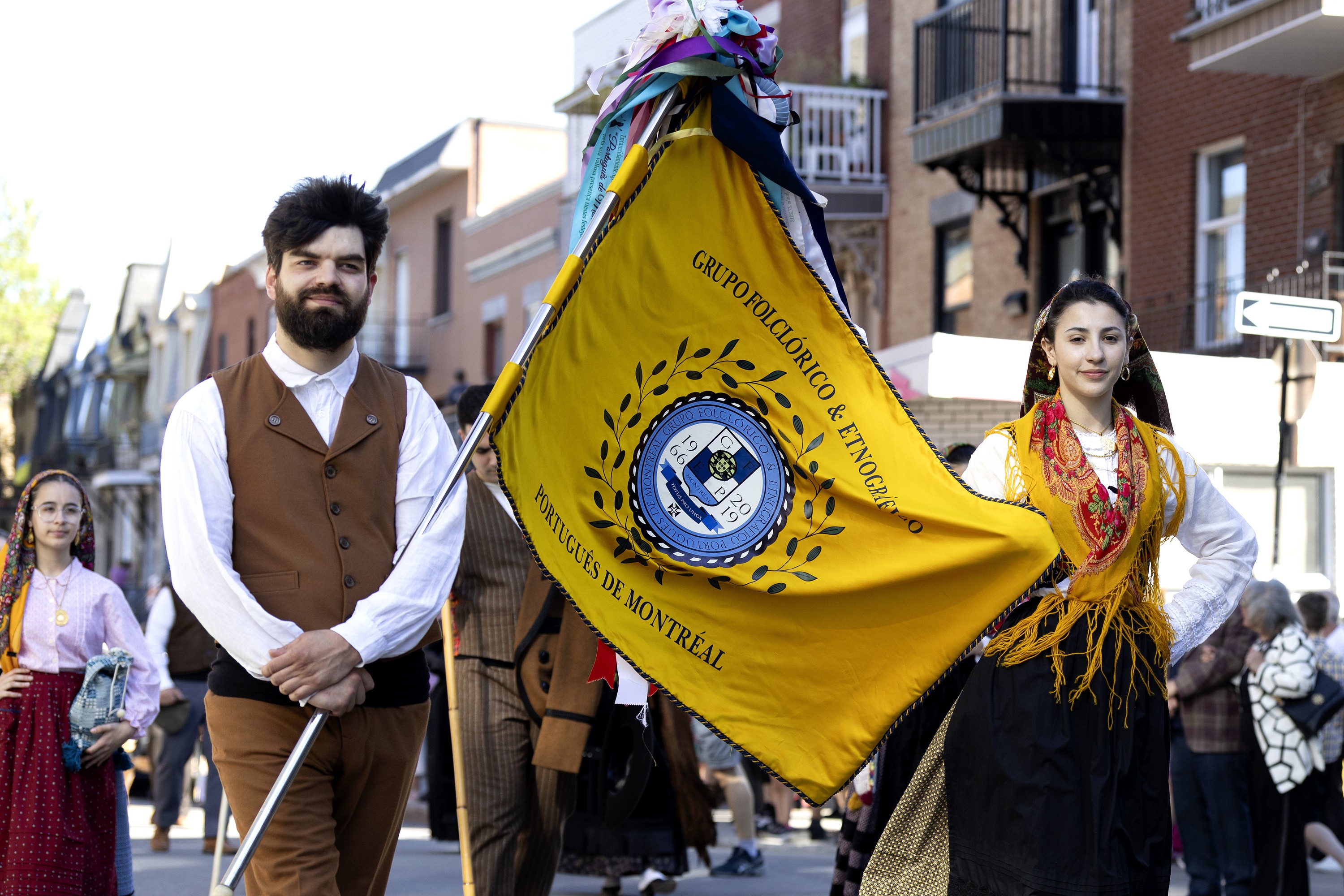 Two people in a procession, carrying a Portuguese community flag.
