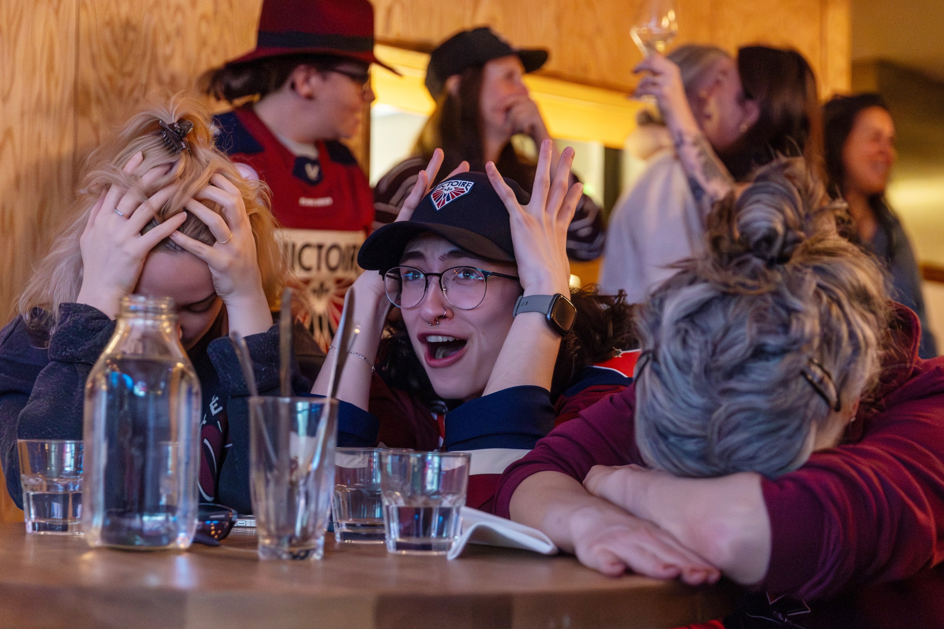 Three women cover their heads as they sit at a table in a bar.