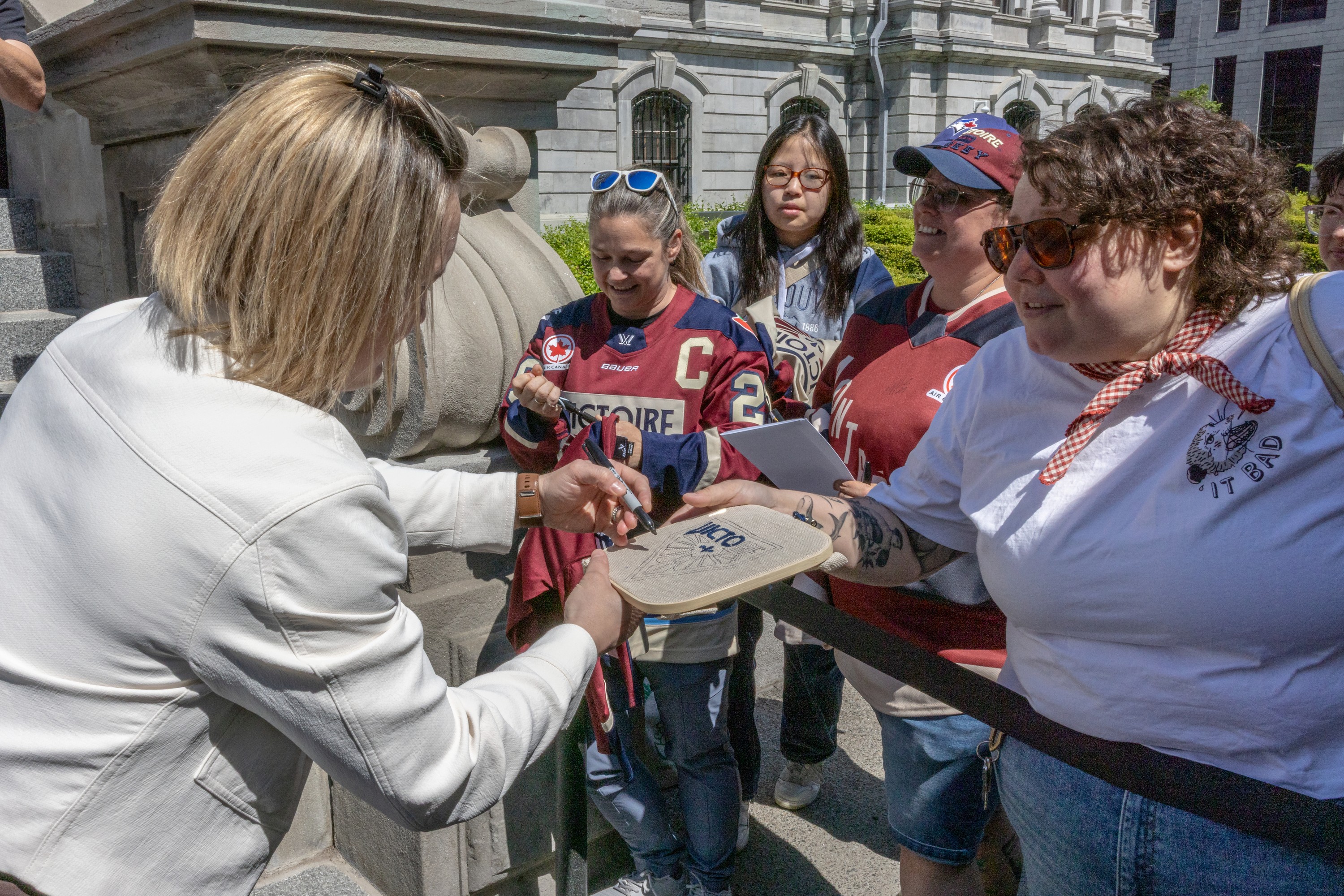 Woman signs an autograph for fan while others look on.