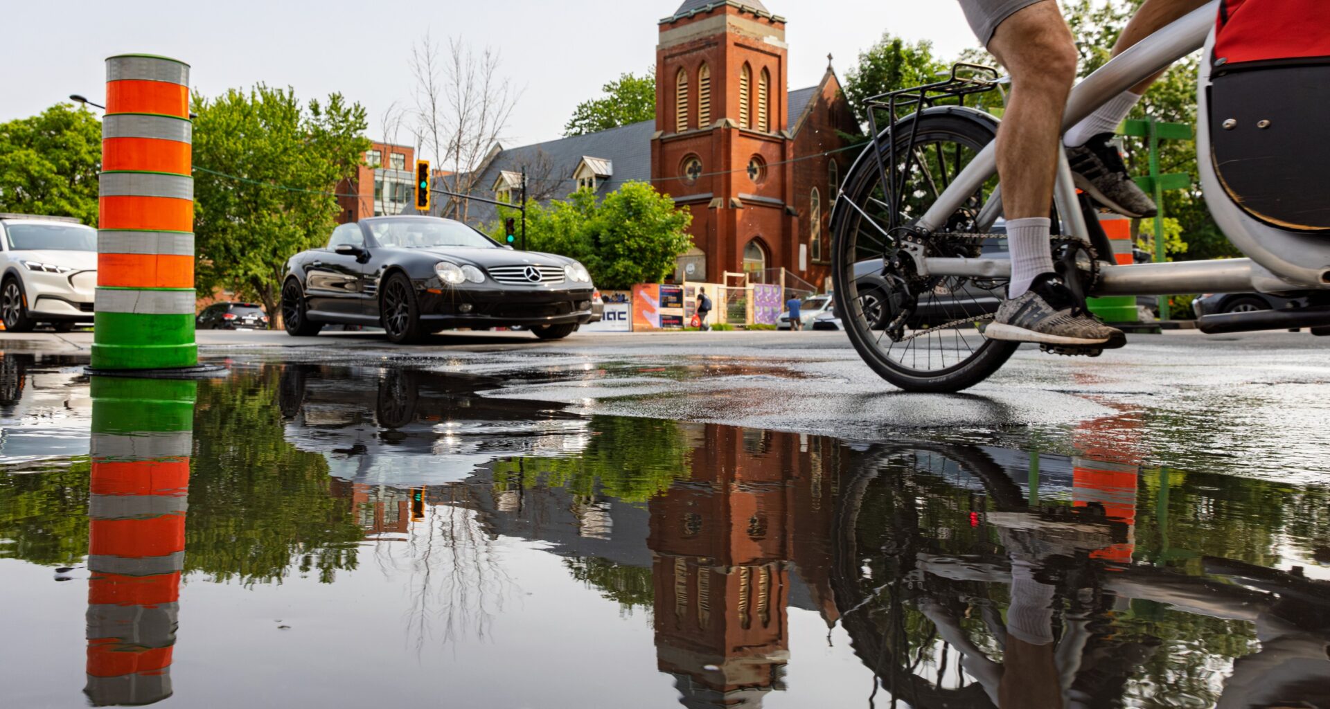 cyclist bypasses large pool of water marked by orange cone on a Montreal street.