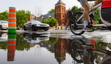 cyclist bypasses large pool of water marked by orange cone on a Montreal street.