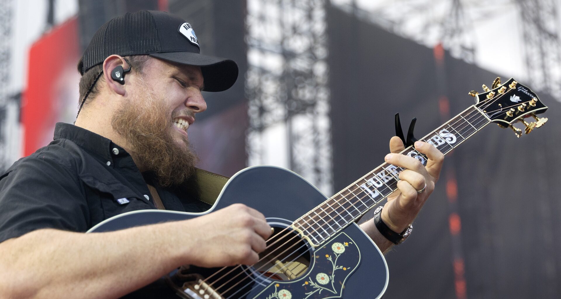 Luke Combs grimaces as he plays guitar.