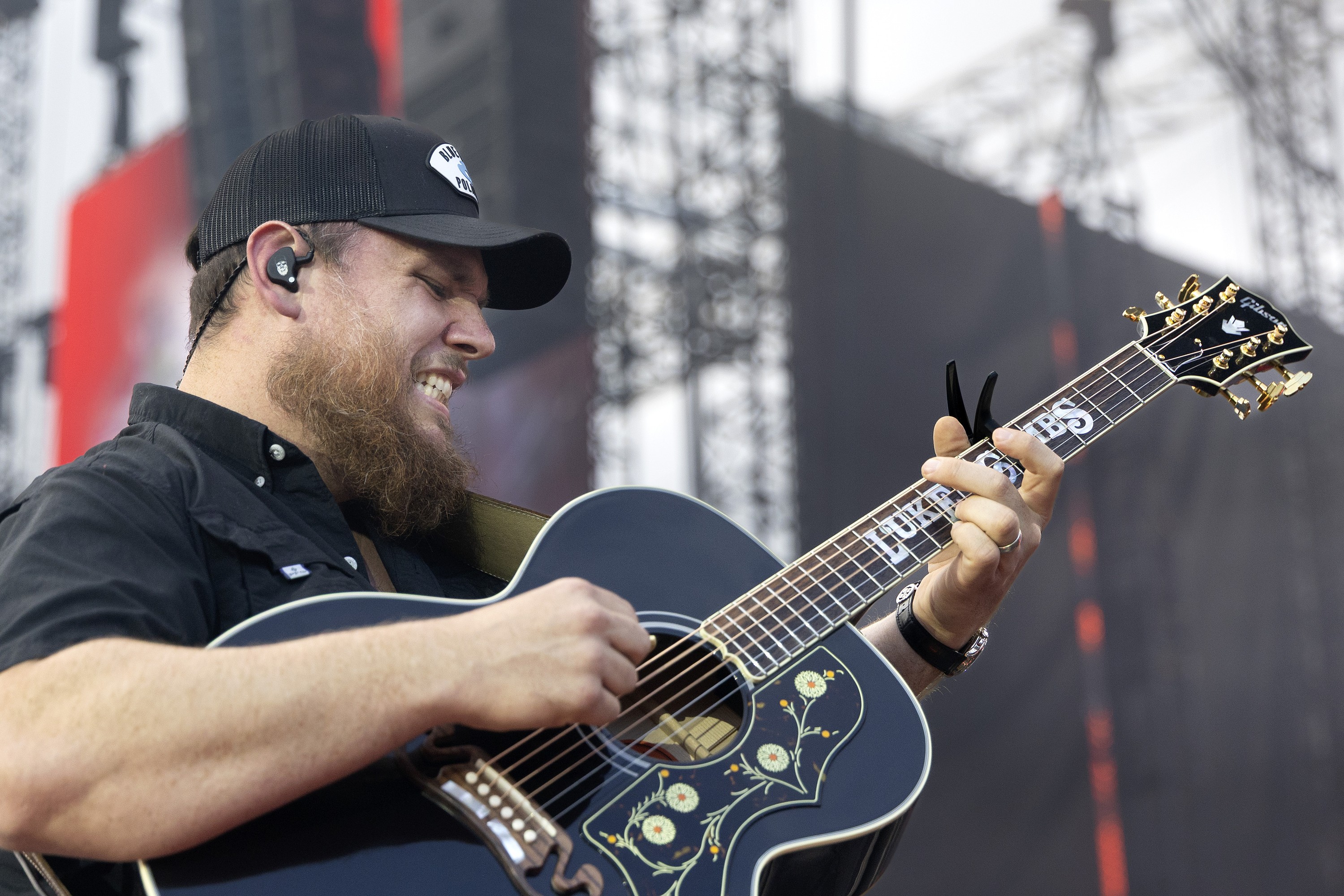 Luke Combs grimaces as he plays guitar.