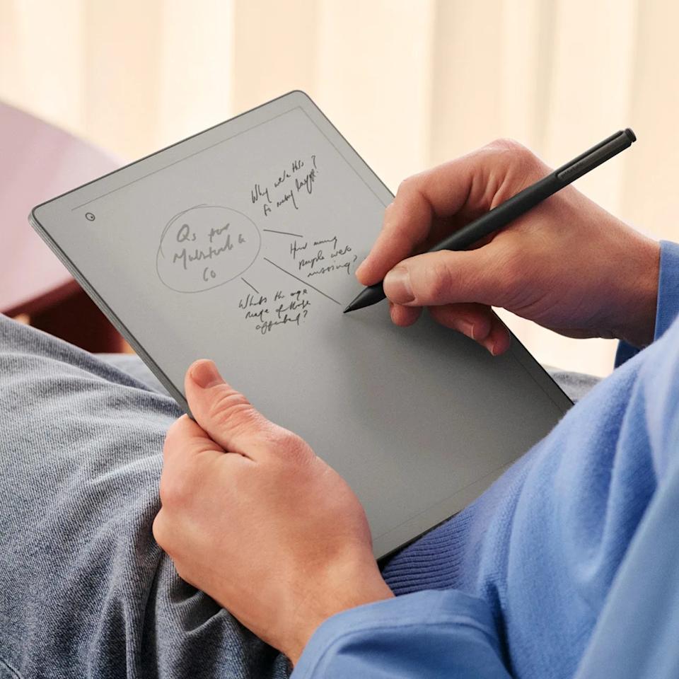 Person holding a gray digital notepad and writing on it with a black stylus pen.