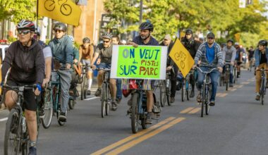 Cyclists on a city street, with one holding a placard that says On Veut des Pistes sur Parc.