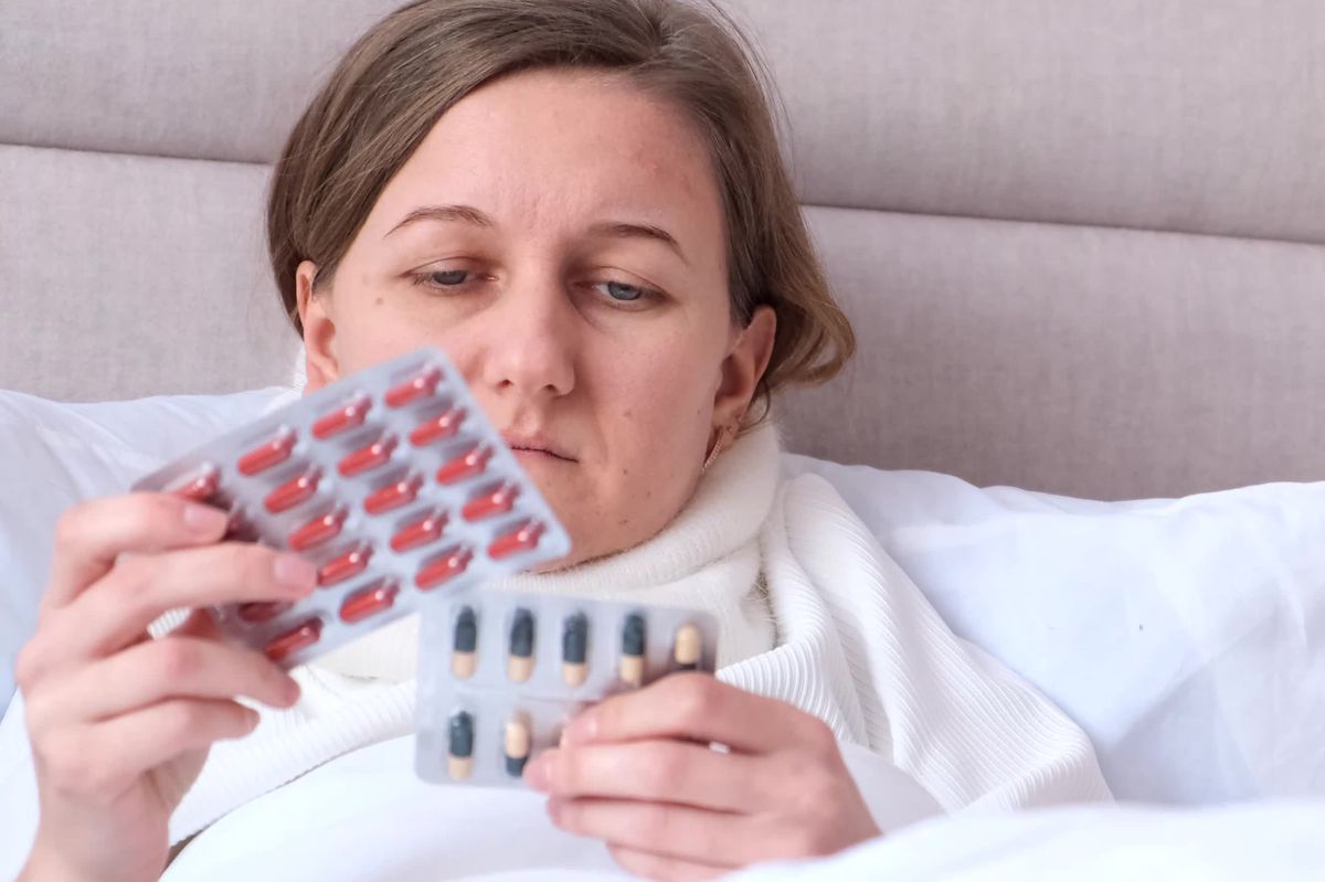 A young woman is lying in bed, she is sick and will drink pills for a cold. Treatment of influenza virus.