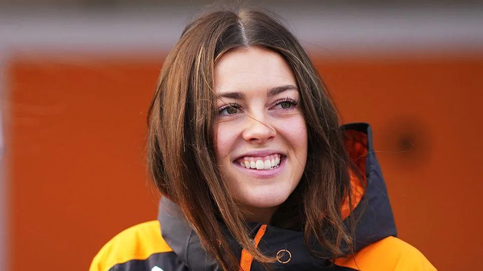 Ella Stevens smiling while wearing a black and orange raincoat.