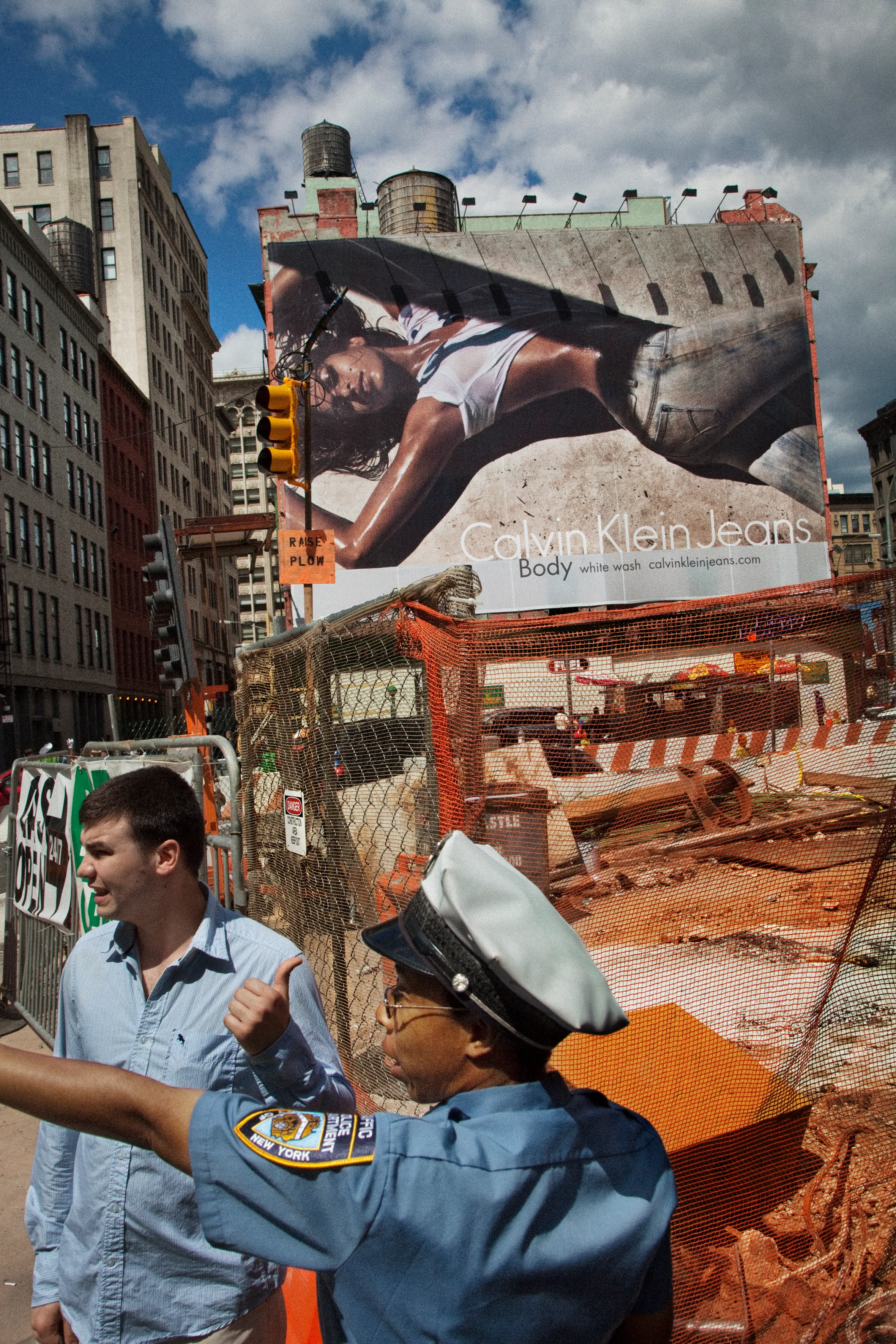 A construction site in Manhattan, New York City, with a large Calvin Klein advertisement and a police officer directing a man.