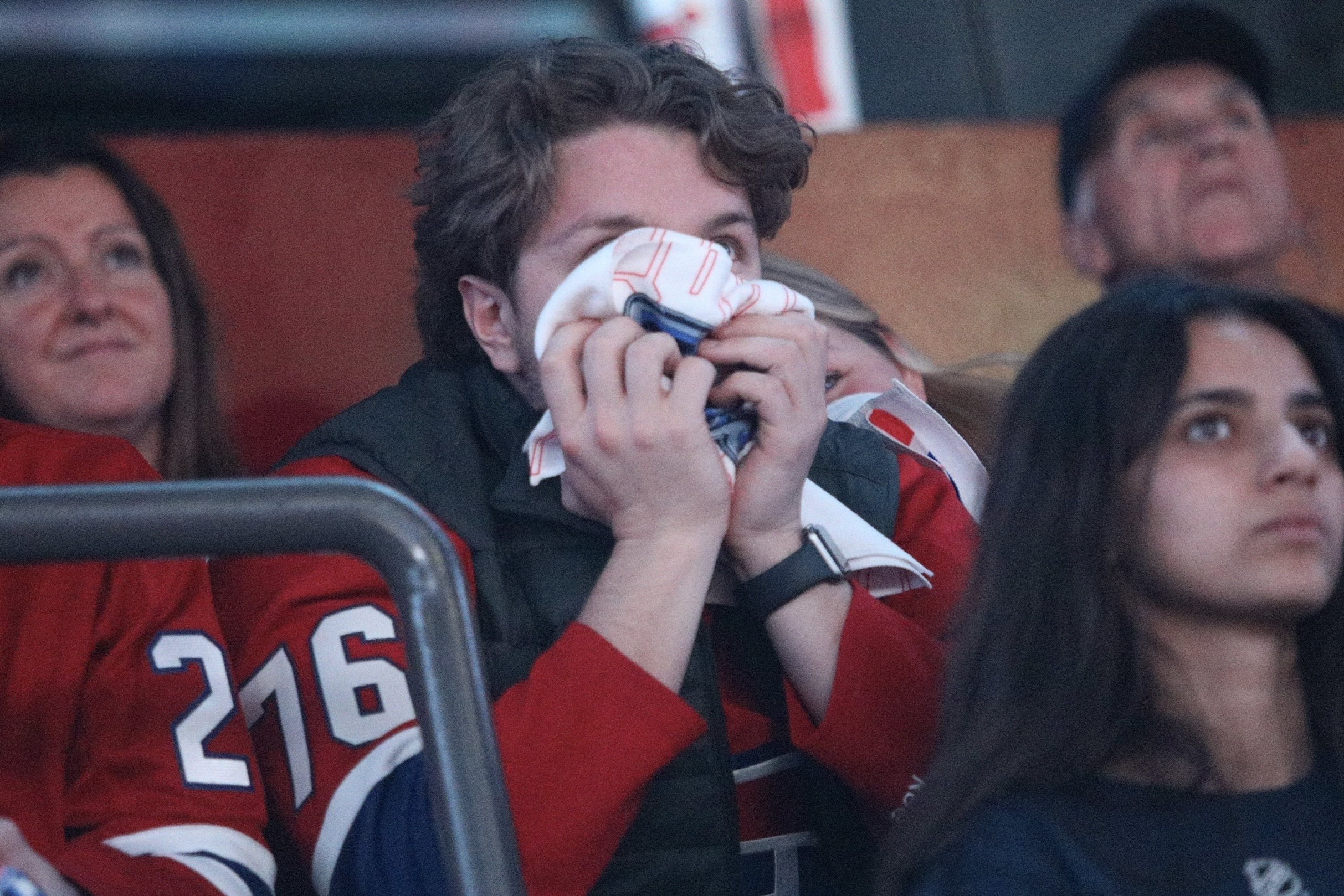 A Canadiens fan clutches a wadded-up item in front of their face while watching the game