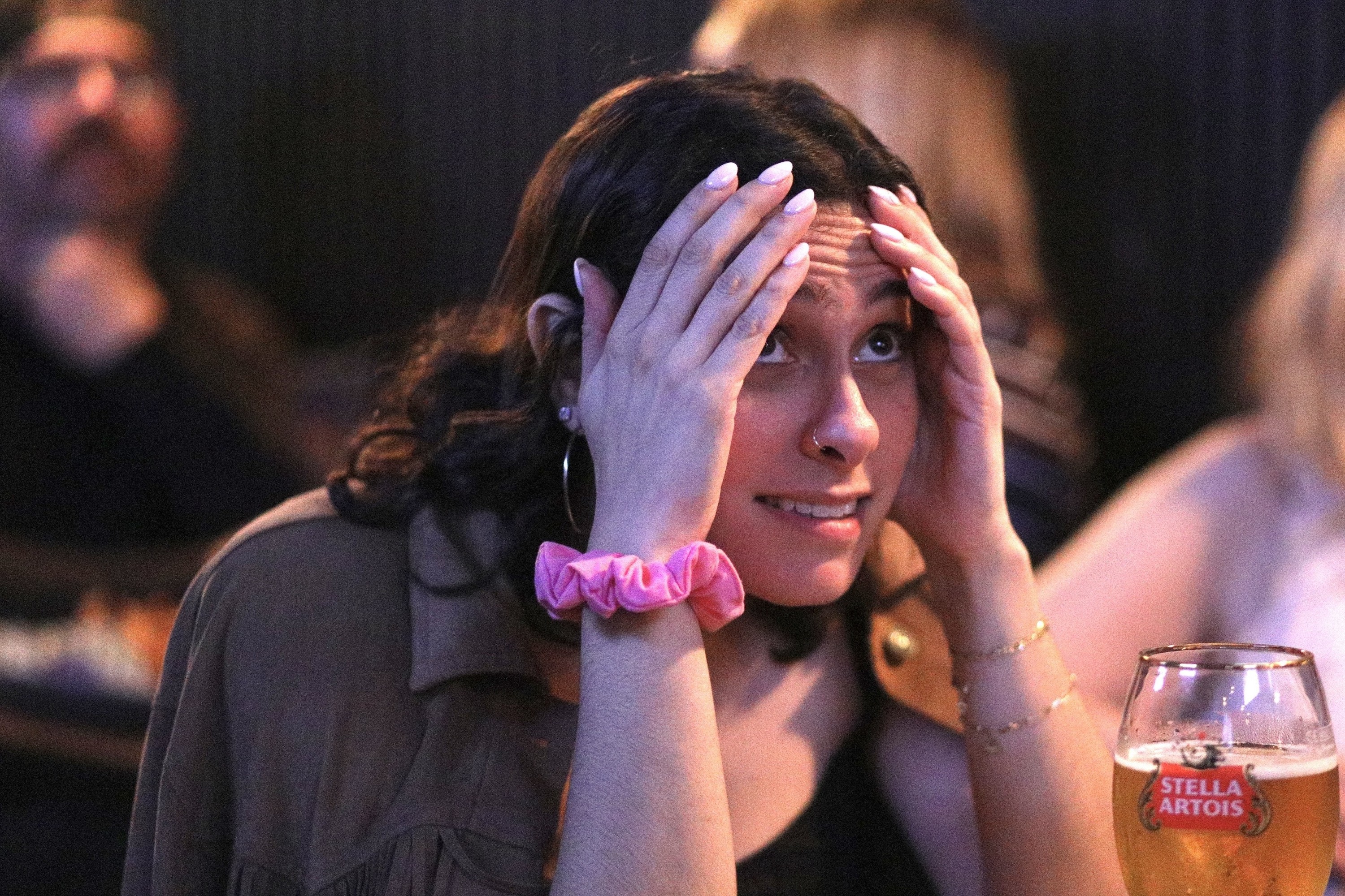 A hockey fan holds her hands on her head while watching a game at a bar.