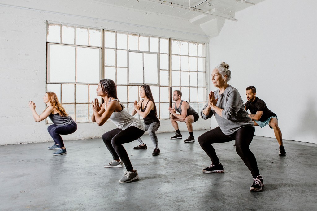 A diverse group of men and women of different ages doing squats in a workout class.