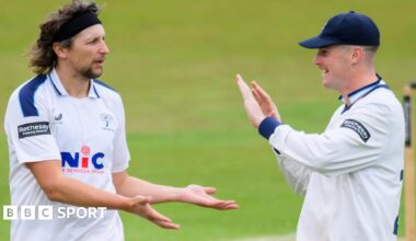 Jack White, wearing cricket whites, gives a low five to another Yorkshire player