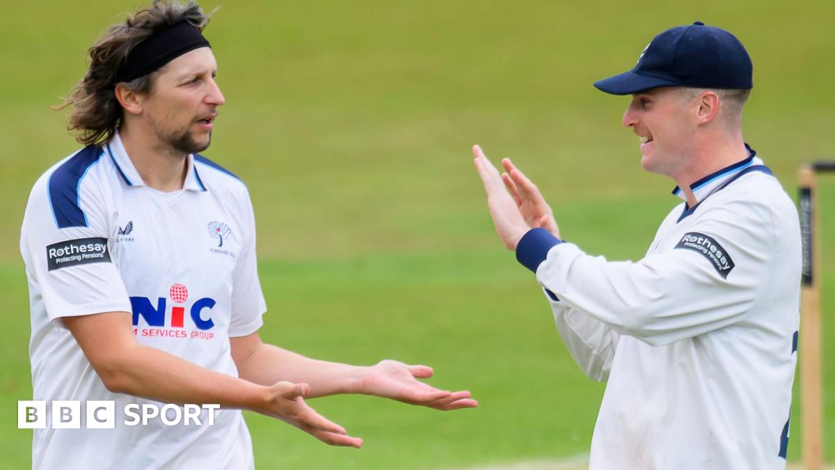 Jack White, wearing cricket whites, gives a low five to another Yorkshire player