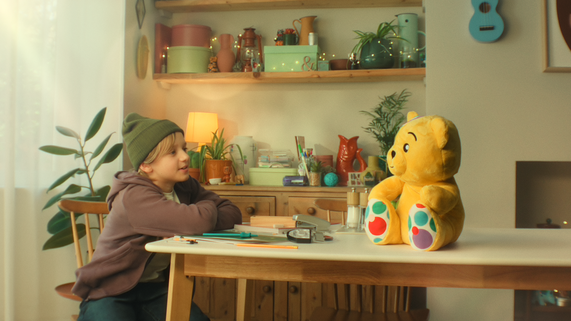 Dexter Sol Ansell seated at a table talking to Pudsey Bear, which is sitting on it