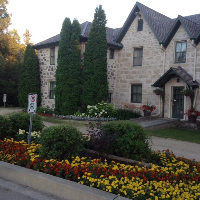 The exterior of a historic stone house surrounded by a flower garden.