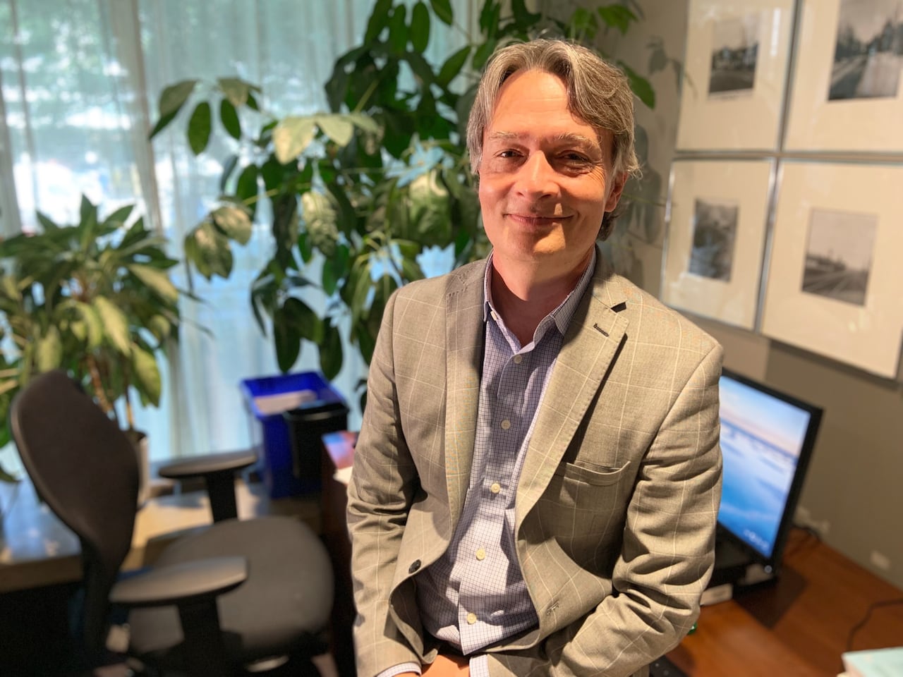 A man in a suit sits on his desk posing for a photo.