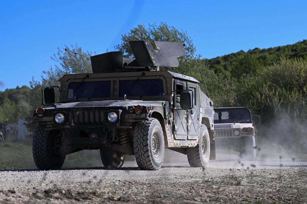 Two military vehicles driving along a dusty road.