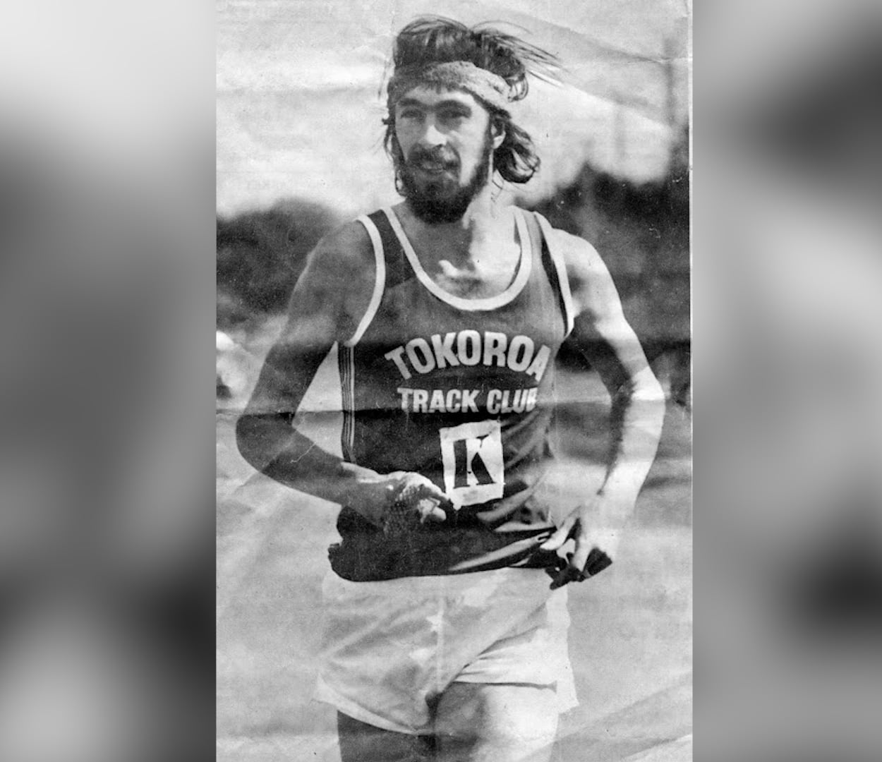 A man running in a sweat band, in a black and white photo.