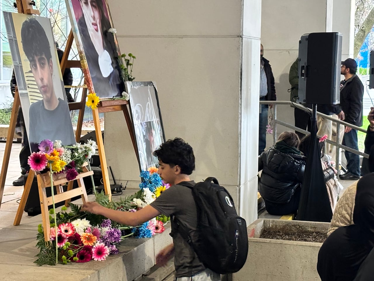 A young person leaves flowers at the bottom of portraits of a teen boy.