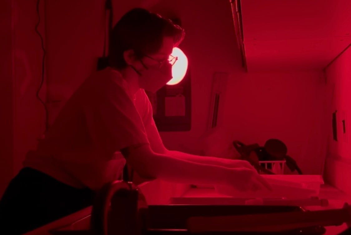 A redish photo of a person in a dark room developing film.