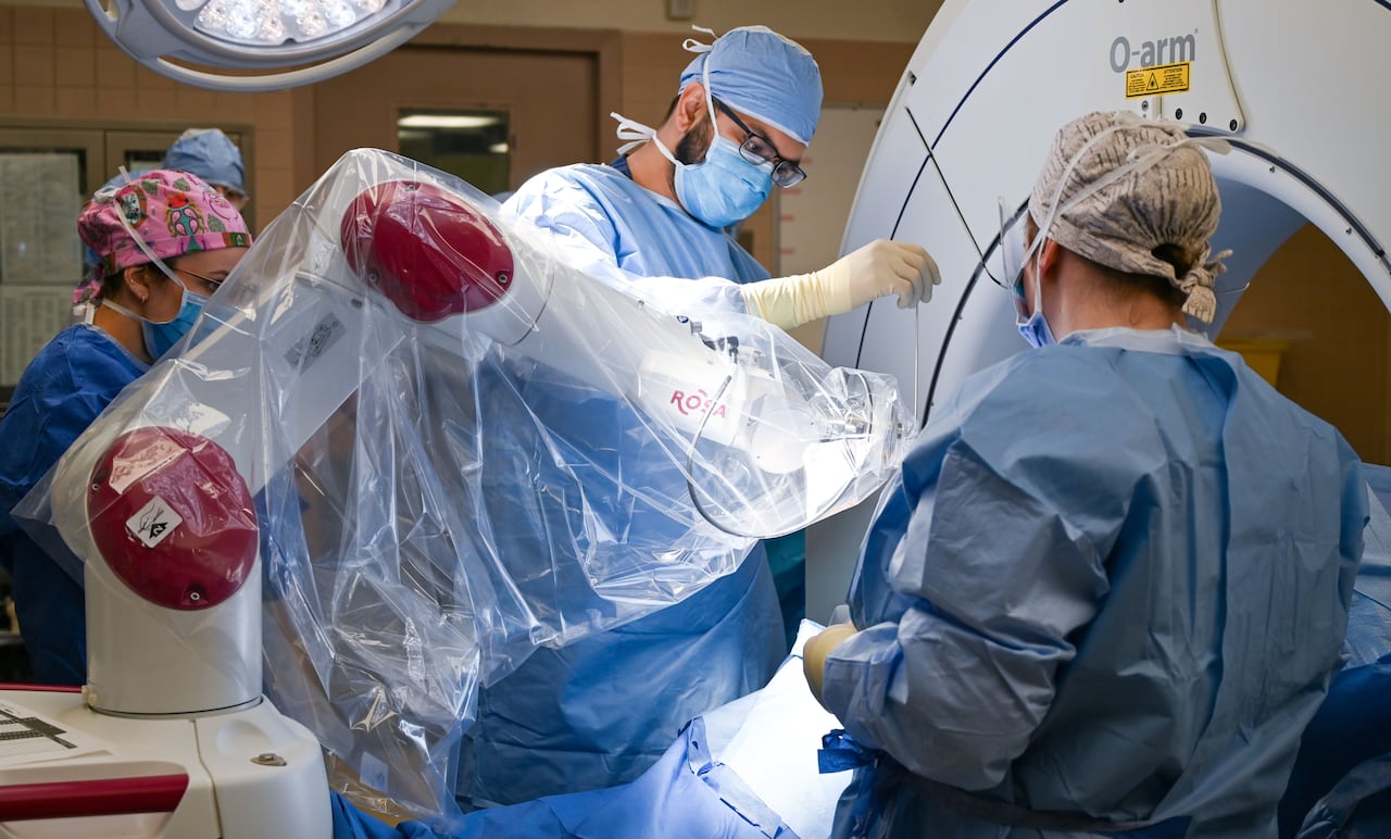 Medical staff in a hospital room with a large robotic arm draped in plastic work on a patient.