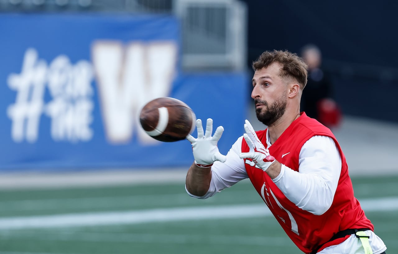A flag football player in a red singlet and white long sleeved shirt catches a football