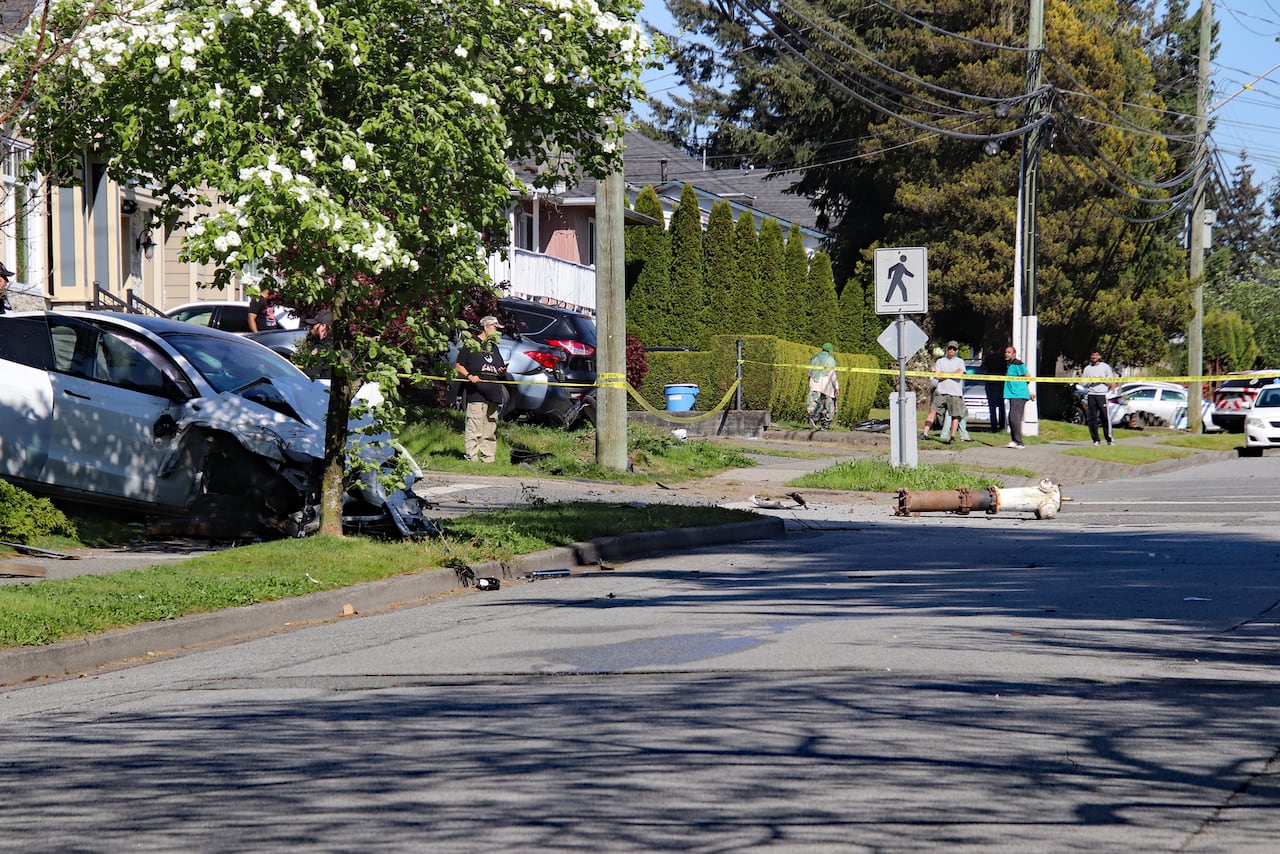 A white Tesla can be seen with the front end caved in. A fire hydrant is sitting laying on the roadway with police tape up around the crash.