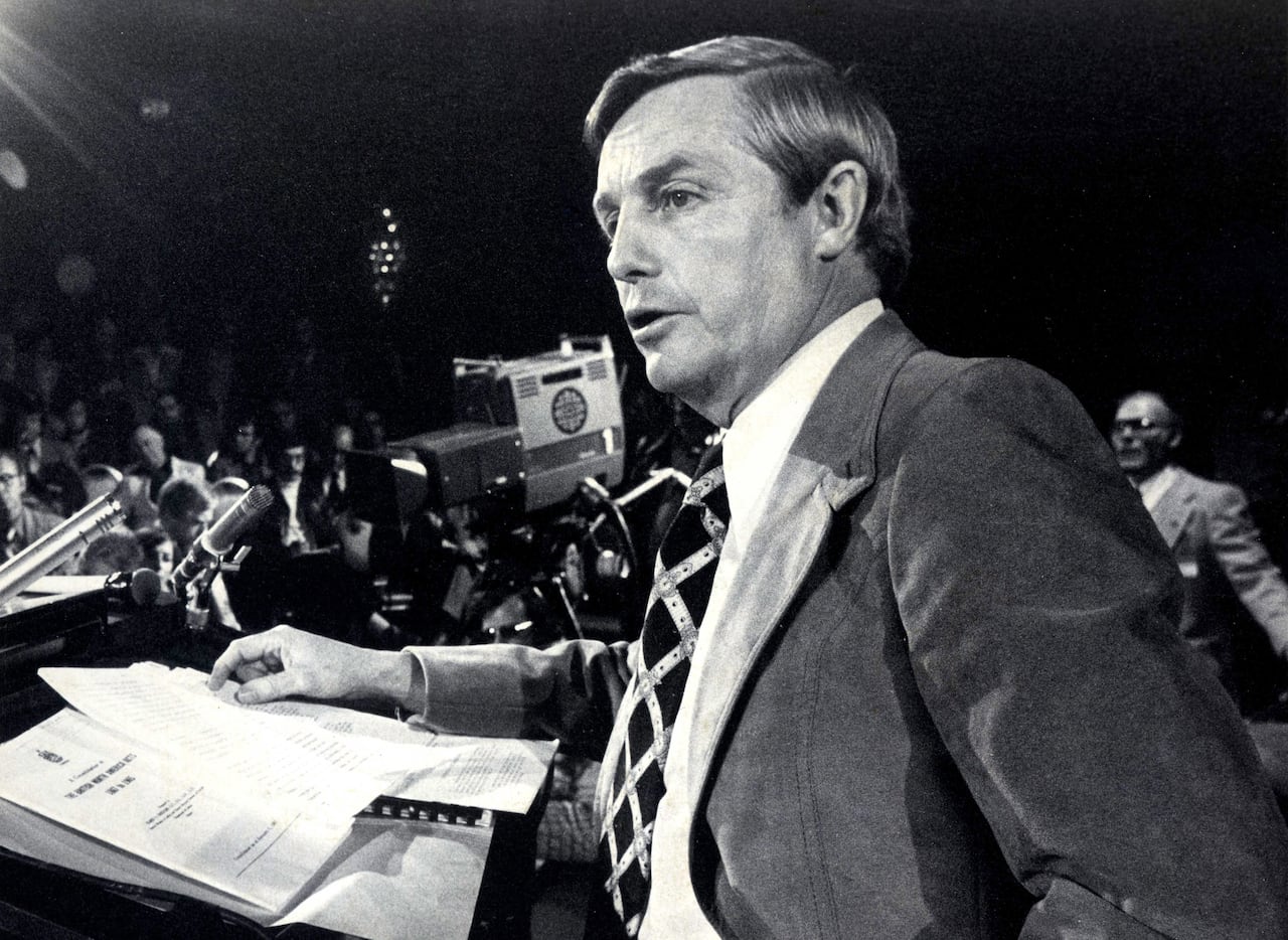 A black and white photo of the Premier speaking in front of journalists.