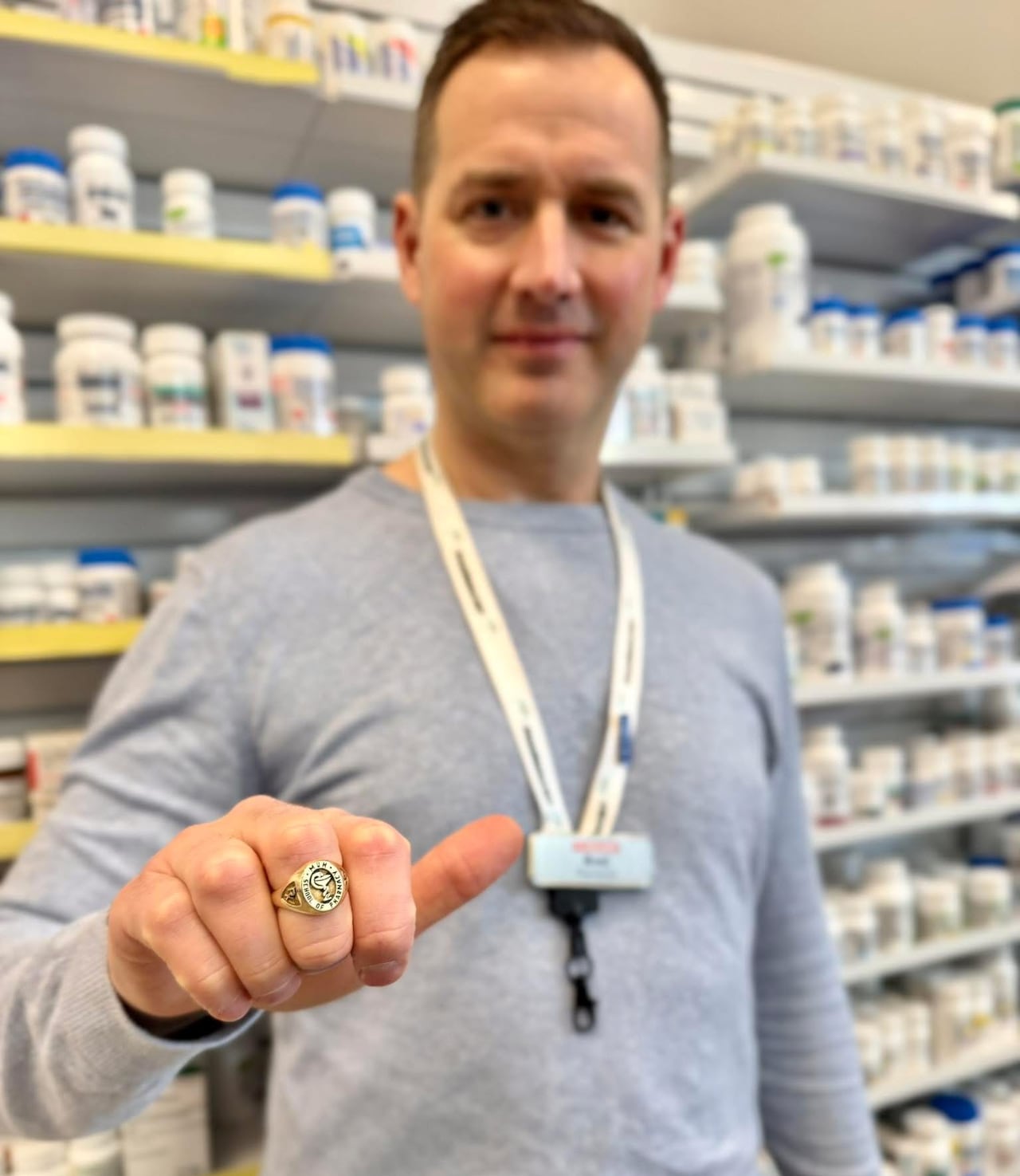 A man standing in a pharmacy, showing the camera a golden ring on his finger.