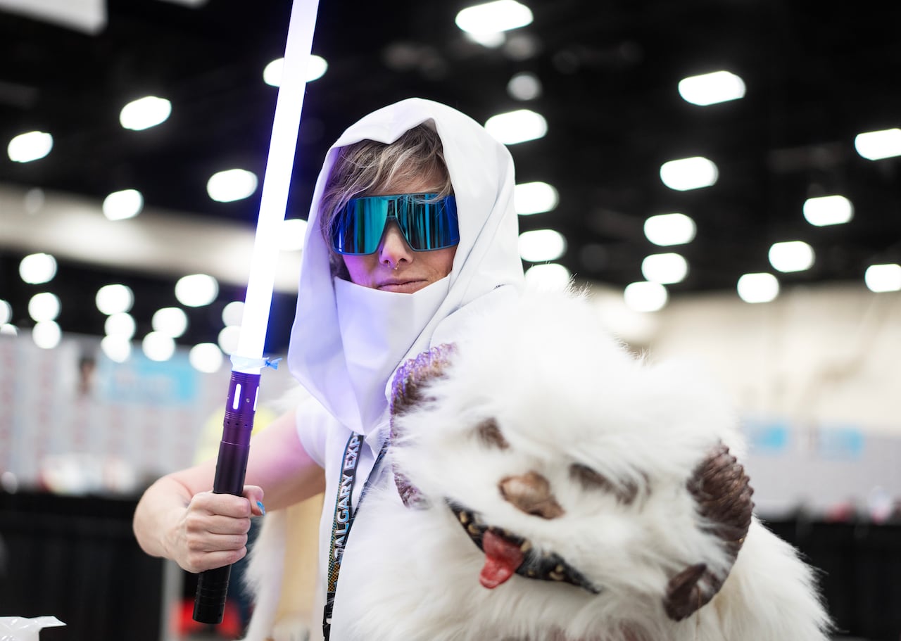 A person holds  a lightsaber and a white plushie.