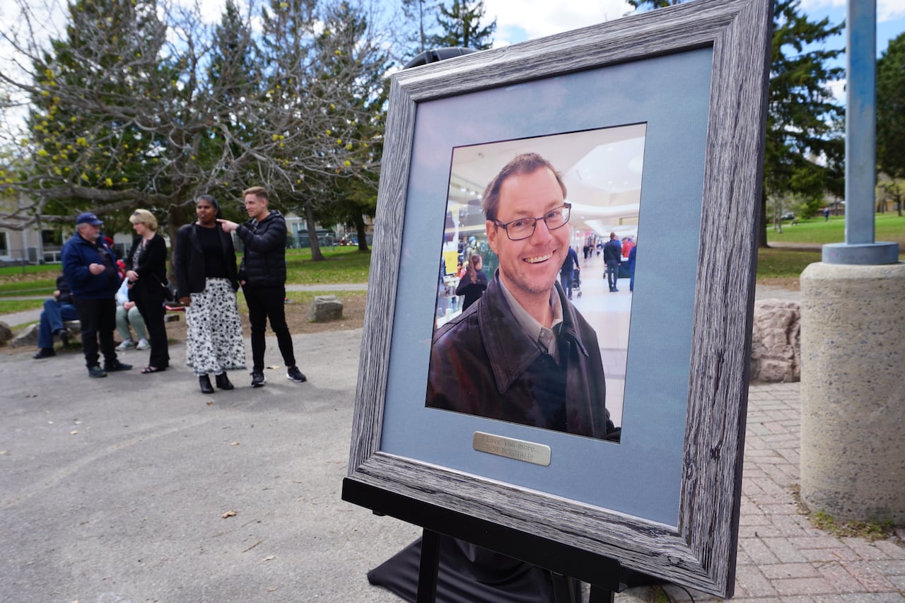 A framed photo of a smiling man on a stand in a park