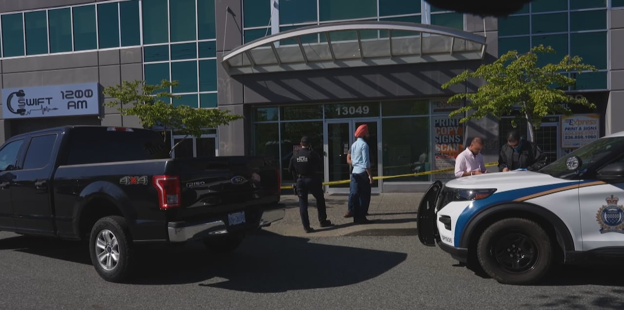 Police cars and crime tape surround the entrance to a building, with officers visible.