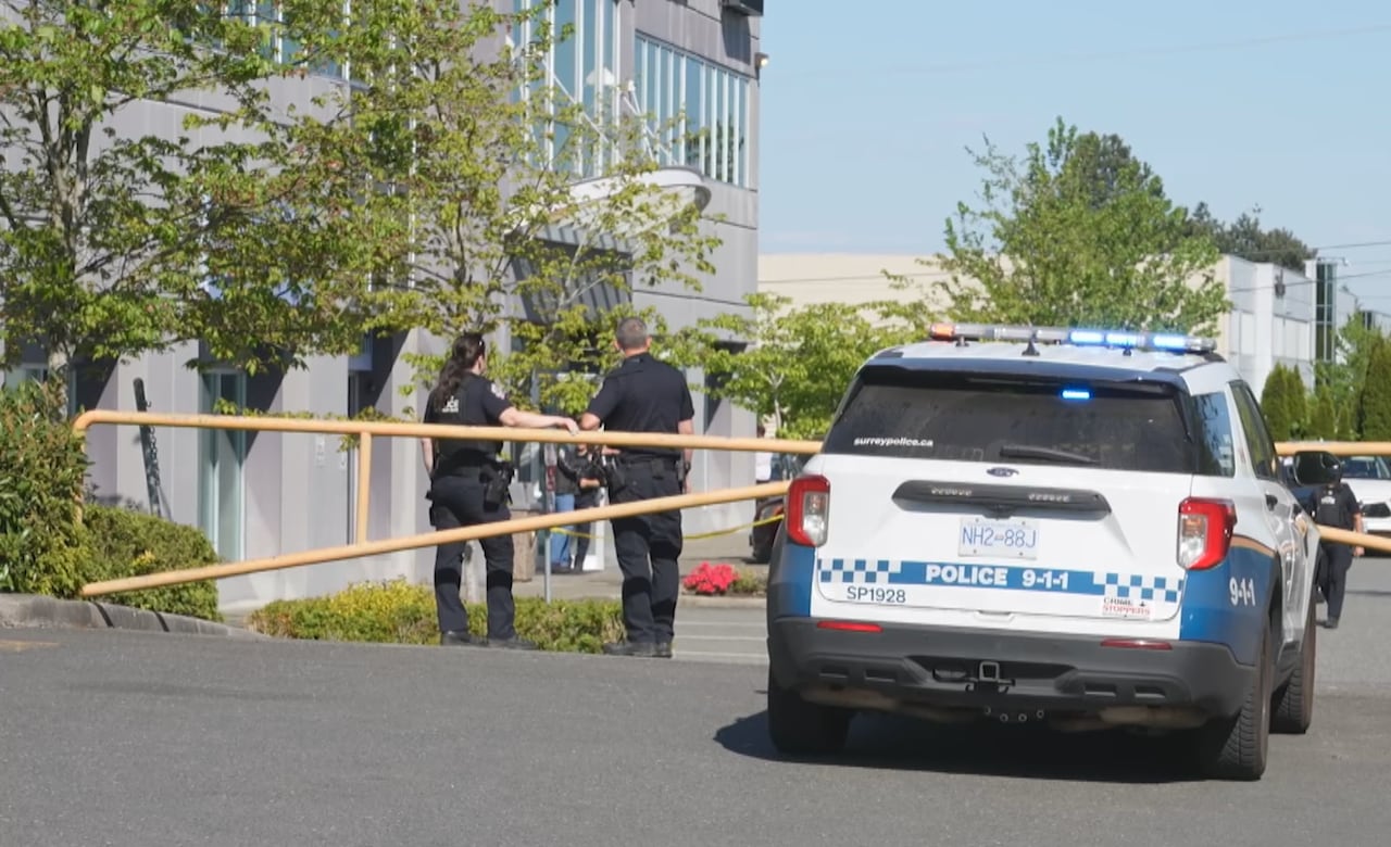 A police car and two officers are seen next to a vehicle barrier on a sunny day.