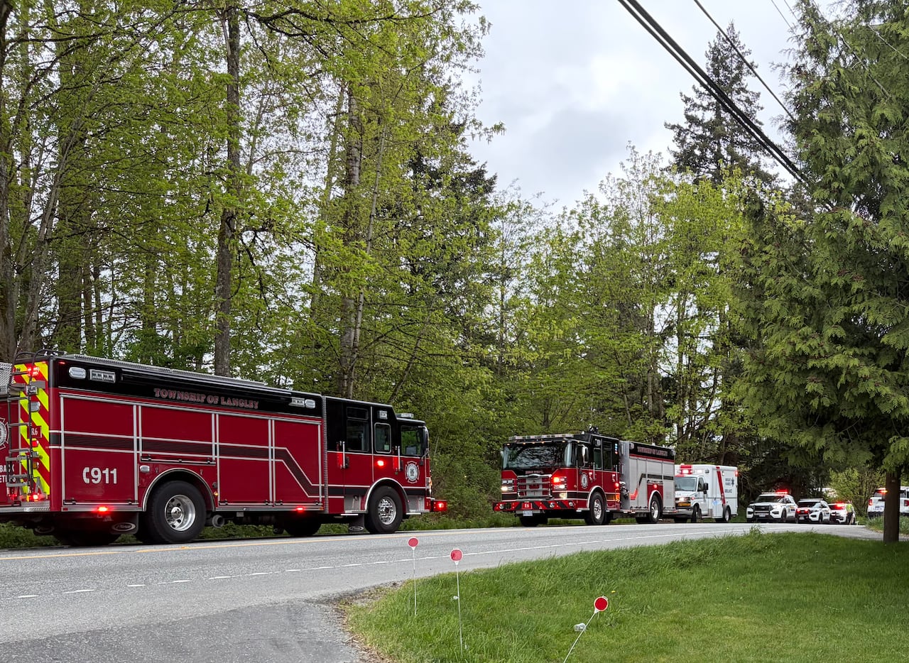 Fire trucks and police cars are parked with lights on on a road.