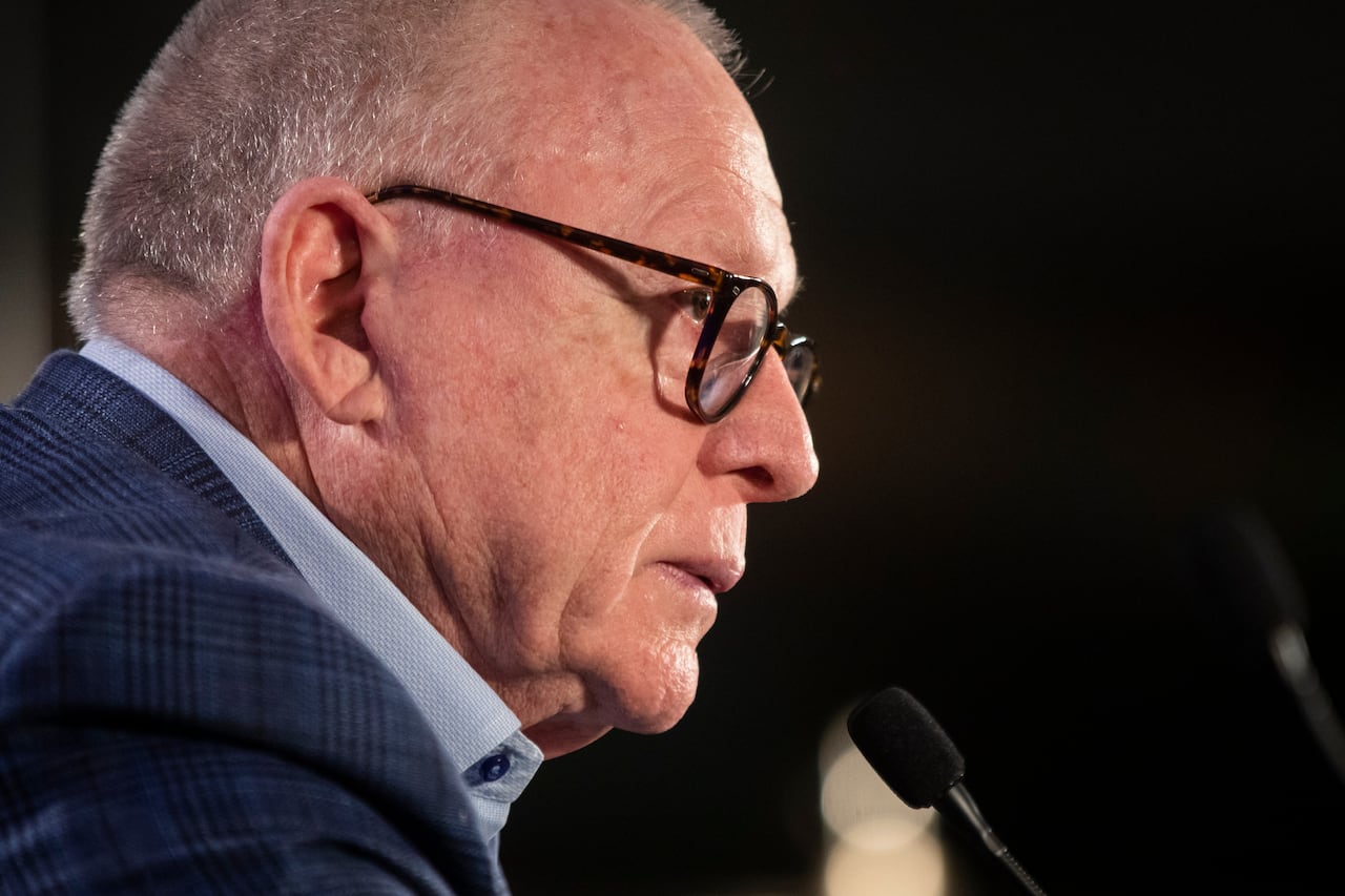 A white man wearing glasses and a blue shirt is pictured speaking to a mic in profile.