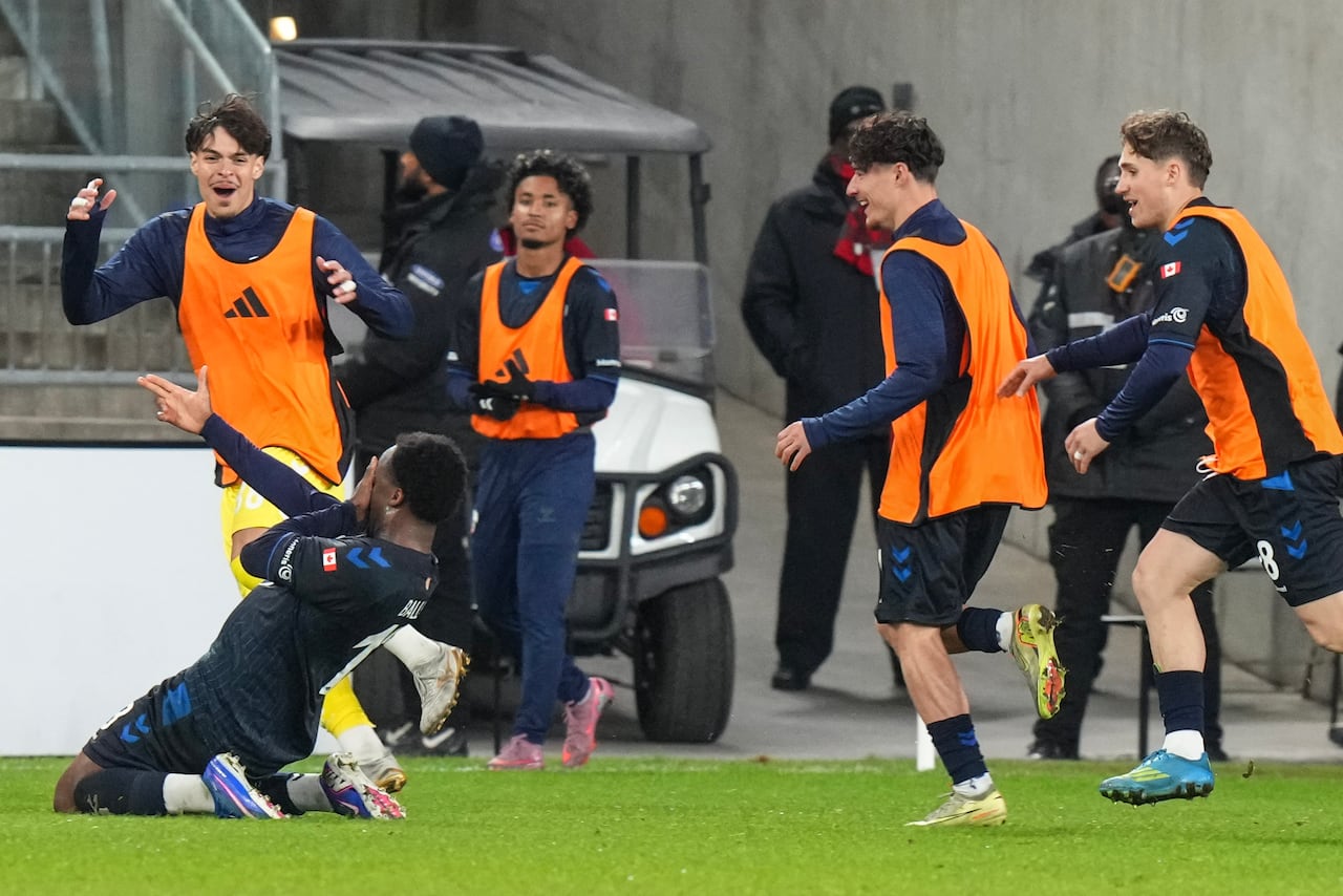 A soccer player slides on his knees to celebrate a goal while happy teammates run behind him.