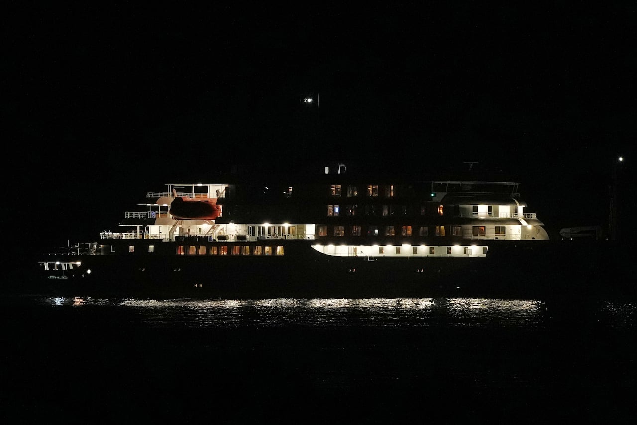 A nighttime scene shows a ship with some lights on cabins and others off.
